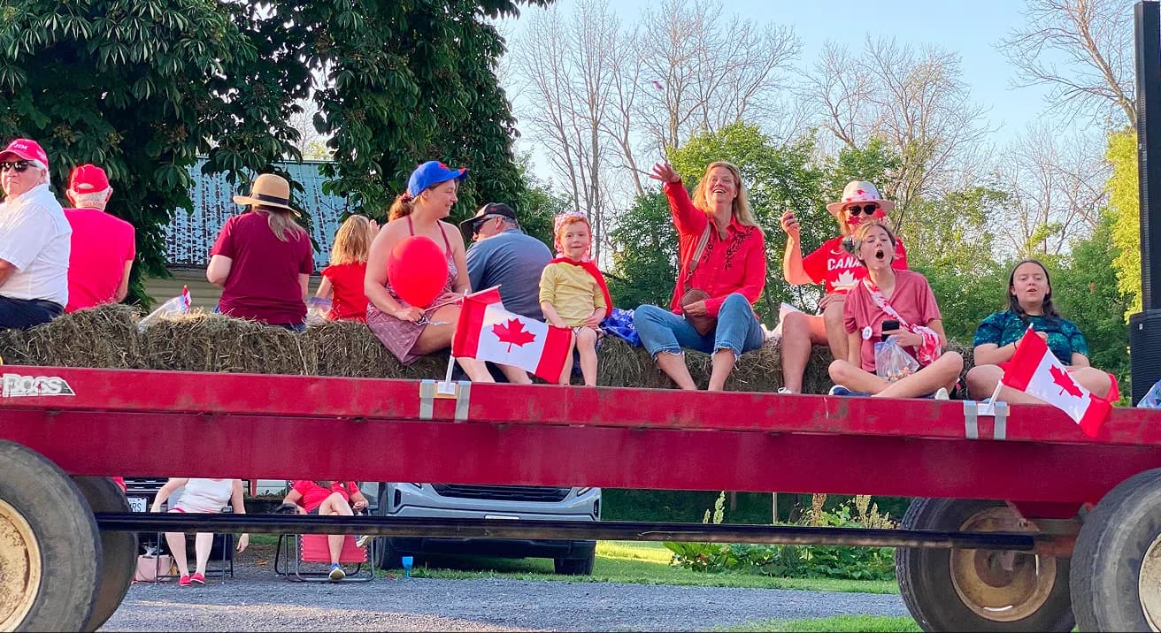 Families on a hay wagon waving Canada Day flags at the Fairgrounds